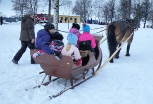 Lapsia ja aikuisia lumisessa metsässä, koira vetää pulkkaa