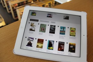 Käsi pitelee tablettia, jolla näkyy e-kirjojen kansia