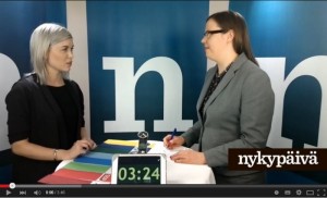 Susanna Koski hymyilee vaalivideollaan, taustalla Suomen lippu