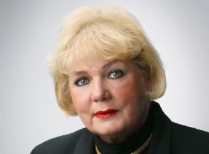 Anne Jääskeläinen puhumassa, taustalla vaalea seinä