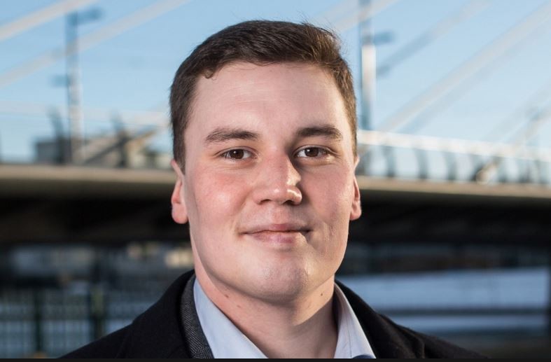 Daniel Lahti hymyilee kameralle, taustalla vaaleanpunainen seinä