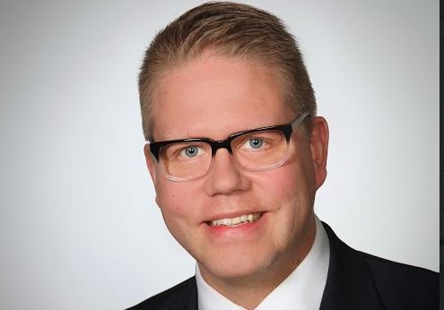 Hannu Makkonen hymyilee kameralle, taustalla Vaasan yliopiston logo