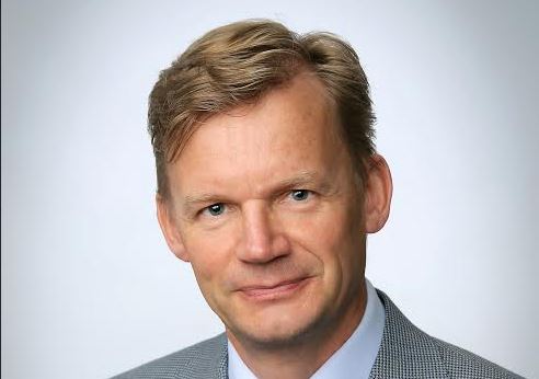 Jari Kuusisto hymyilee kameralle, taustalla Vaasan yliopiston logo