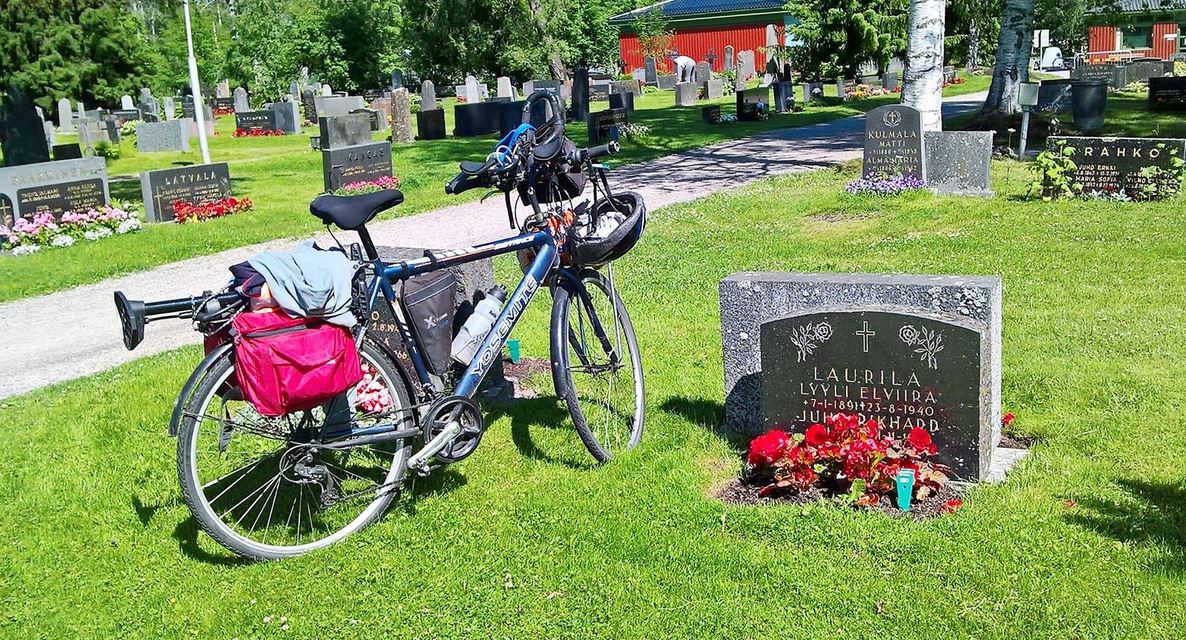 Pyöräilijä polkee maaseudulla, pizza-laatikko tarakalla