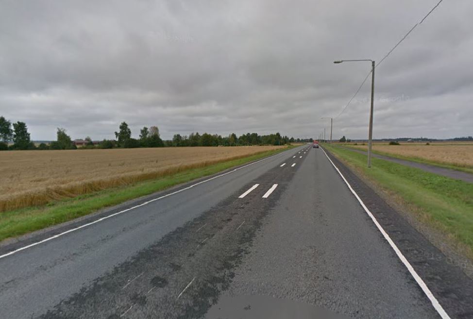 Lakeusmaisema, jossa peltoja ja metsää, taustalla rakennuksia