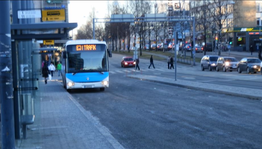 Keltainen paikallisbussi pysäkillä, matkustajia nousemassa kyytiin