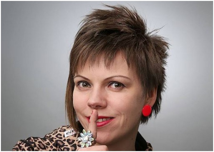 Nainen puhuu mikrofoniin, taustalla puolueen logo