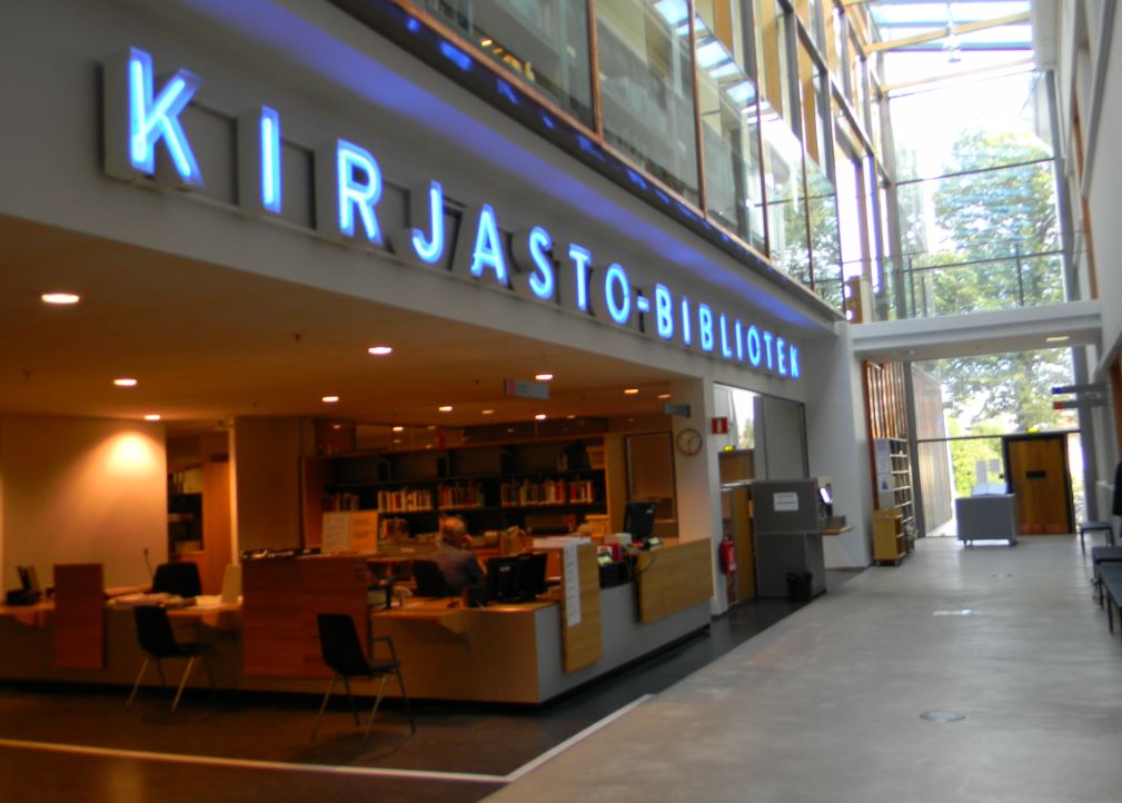 Kirjaston hyllyjä täynnä kirjoja, pöytiä ja tuoleja