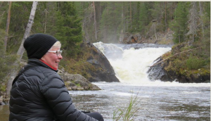 Maire Ruotsalainen hymyilee, taustalla hänen taidettaan