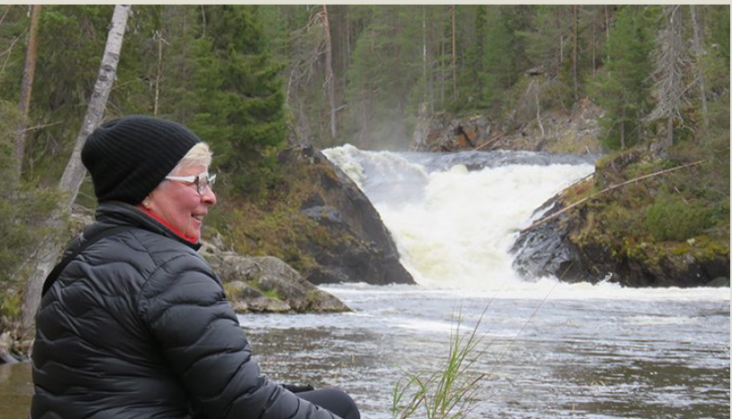 Maire Ruotsalainen hymyilee, taustalla hänen taidettaan