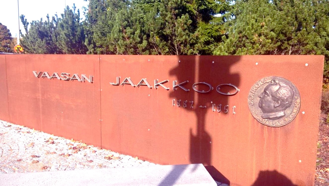 Jaakko Ikolan muistomerkki Vaasassa, taustalla rakennuksia